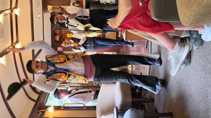 Musicians and dancer performing lively folk music inside a train lounge car.