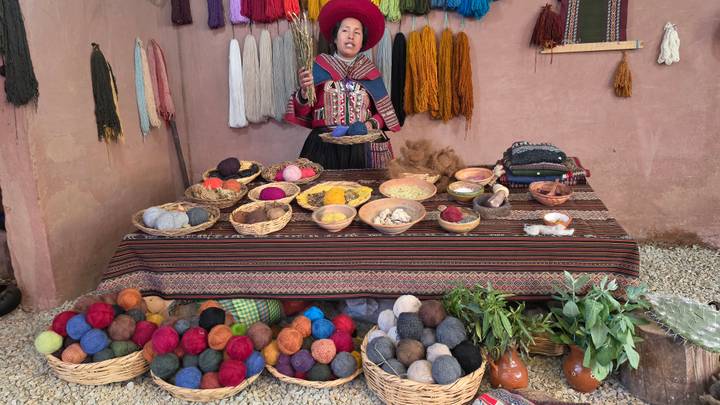 Woman showing baskets of colourful natural dyes and yarn balls on a table in an artisan workshop.