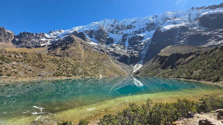 Crystal-clear turquoise Humantay Lake mirroring snow-capped Andean peaks under a deep blue sky.