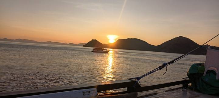 Golden sunset over calm sea with a silhouetted boat and island ridges.