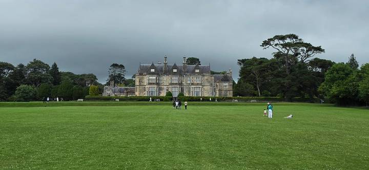 Expansive green lawn leading to stately Muckross House framed by dark clouds in Killarney National Park.