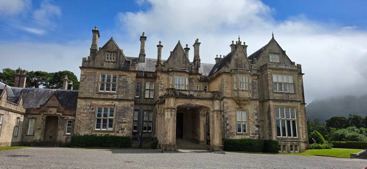Stone manor house with elaborate chimneys set beneath drifting clouds and framed by clipped lawns.