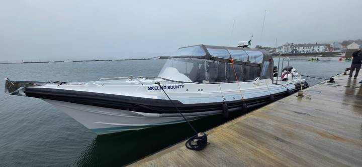 Modern white speedboat named 'Skellig Bounty' moored to a dock on a misty harbour morning.