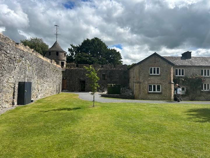 Stone courtyard with turret, cottage and manicured lawn under patchy clouds in Ireland