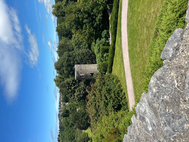 Round stone tower rising above lush green gardens viewed from a castle wall
