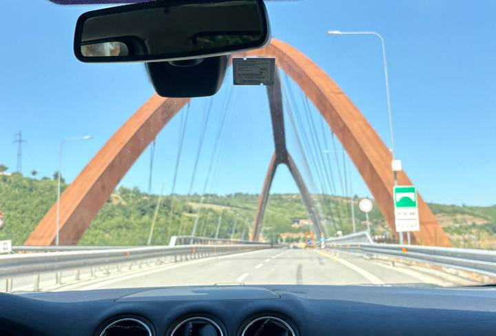 View through car windshield of modern rust-colored bridge arching over highway.