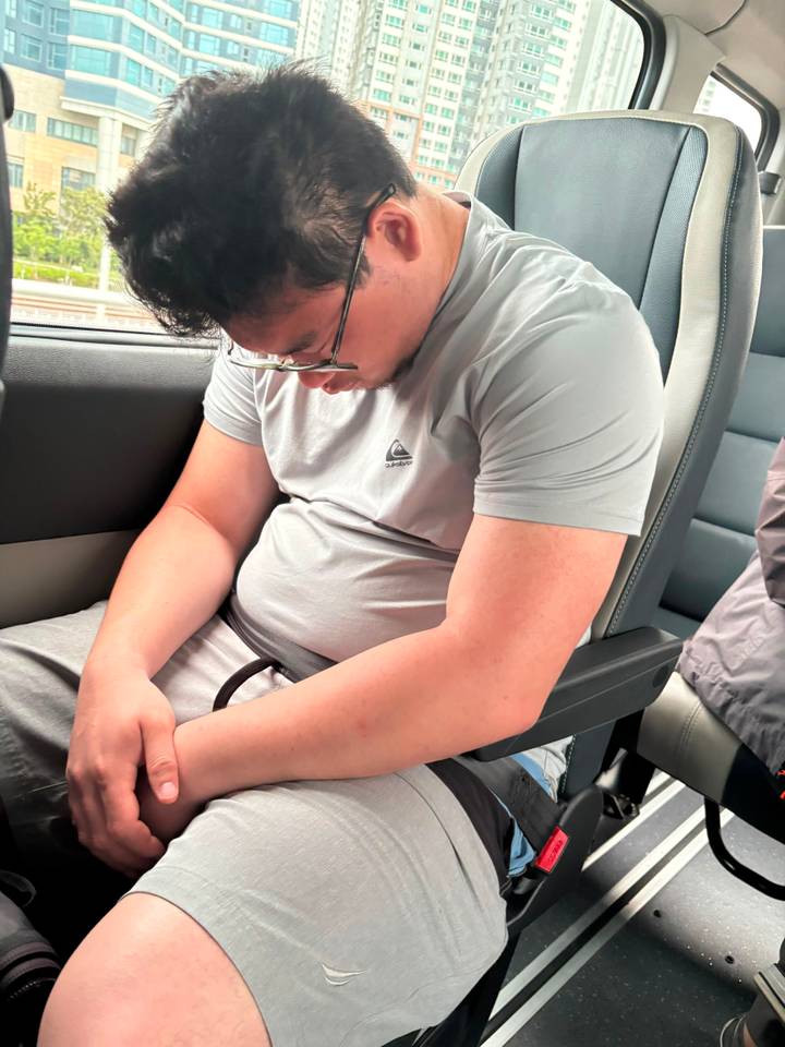 Man naps in a vehicle seat with head down wearing glasses and grey clothes