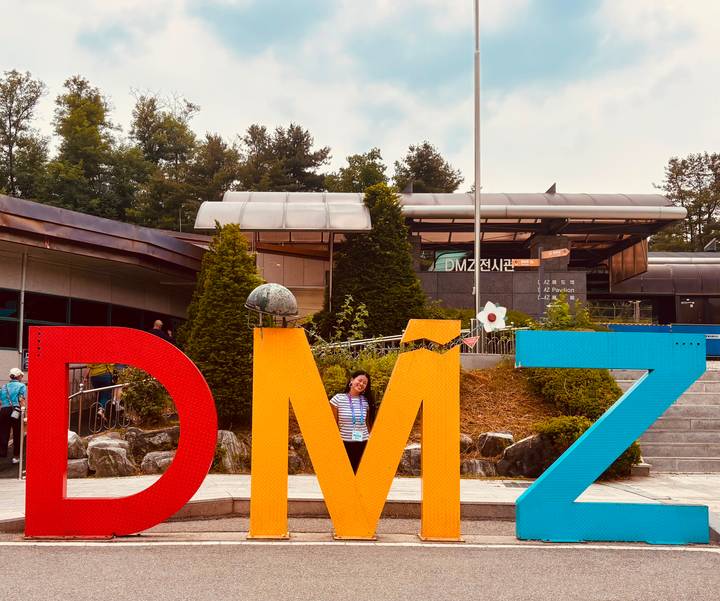 Traveller stands smiling inside the large colourful 'DMZ' sign at an outdoor visitor centre