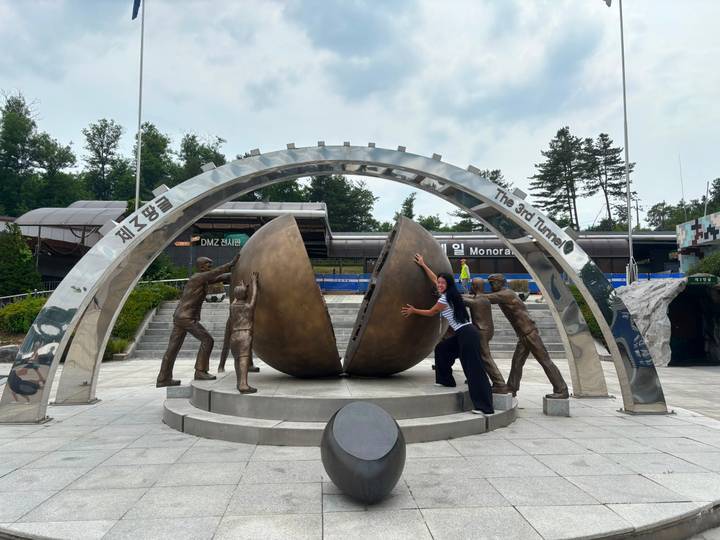 Woman playfully pushes apart two giant bronze doors at the 3rd Tunnel DMZ monument