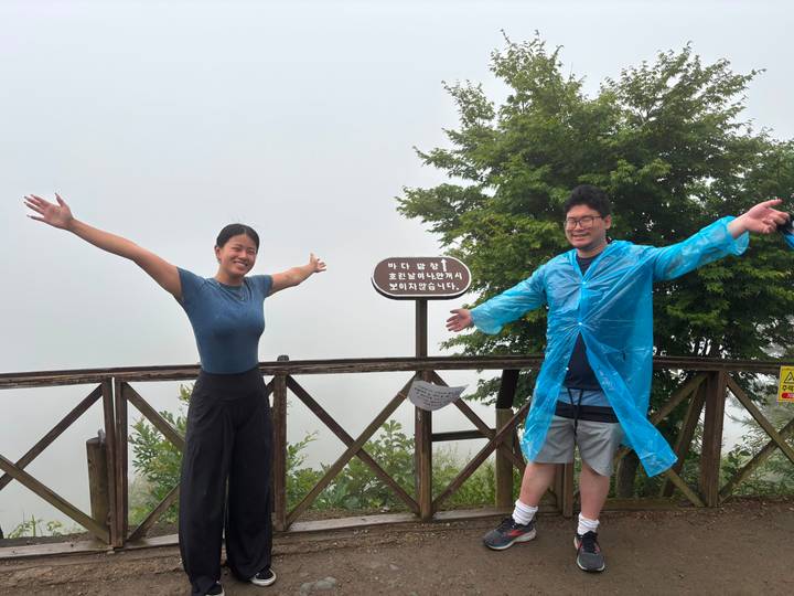 Friends in foggy mountain setting smile with arms stretched wide beside a wooden fence