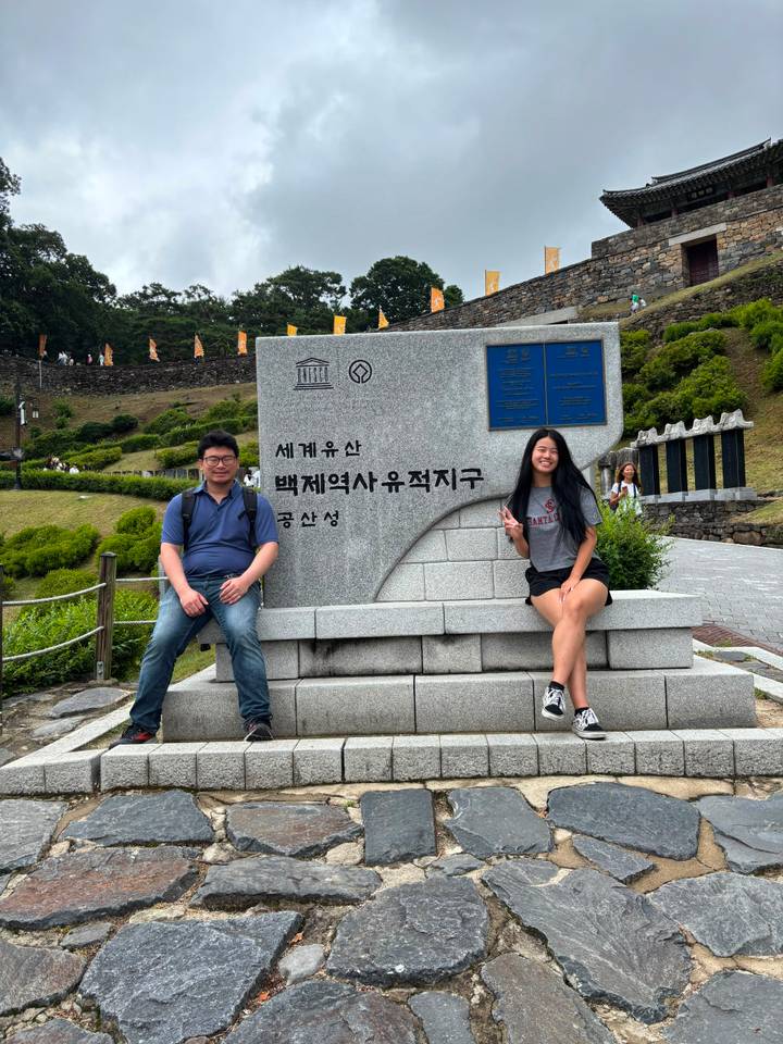 Travellers sit on a stone UNESCO Baekje Historic Areas monument posing for a snapshot