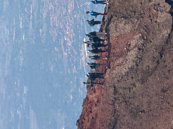 Small hiking group standing on the rim of a reddish volcanic crater high above the valley below.