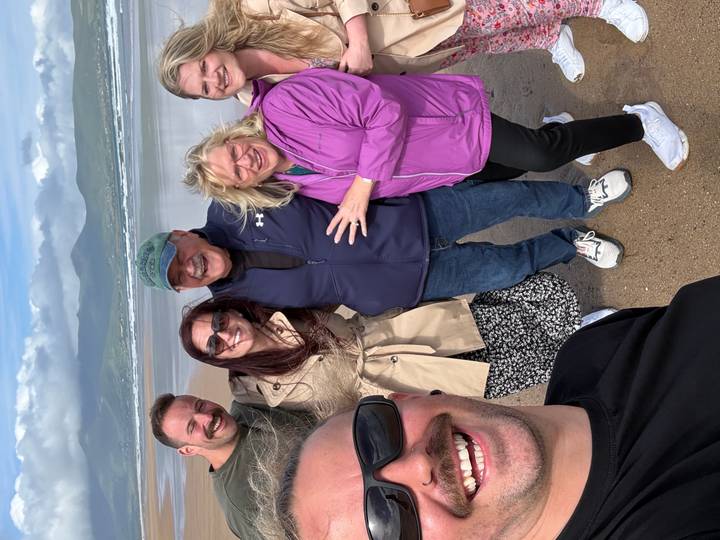 Happy multigenerational group selfie on a sandy beach with distant green mountains and waves