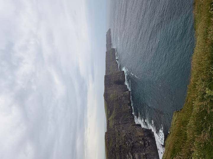 Iconic vertical cliffs plunging into Atlantic Ocean at the Cliffs of Moher under gray sky