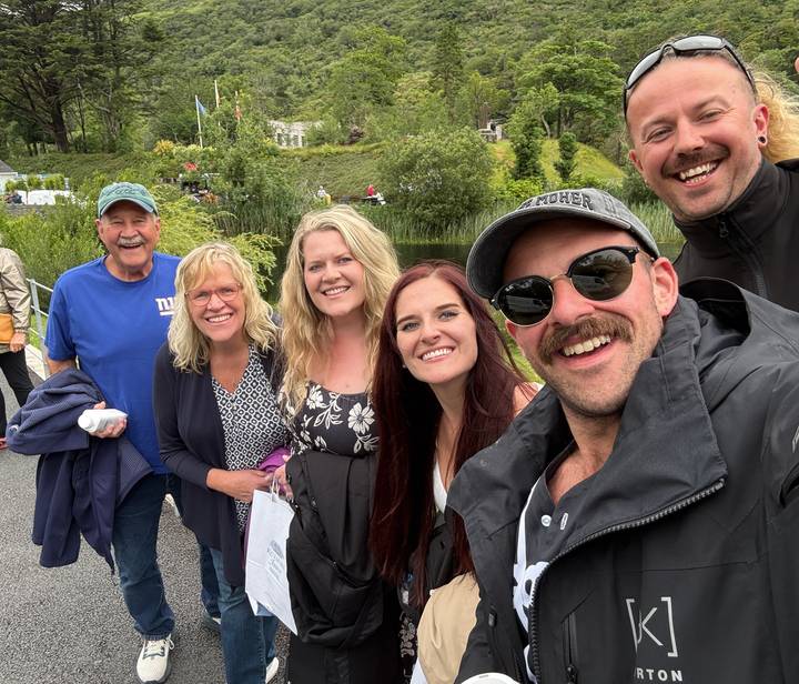Smiling group selfie at landscaped park with pond and lush greenery in background