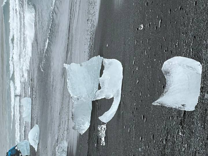 Multiple crystal ice fragments scattered across black sand with breaking surf in the background