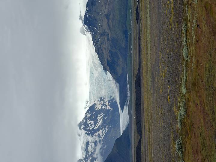 Distant glacier flowing between dark rugged peaks beneath a heavy grey sky