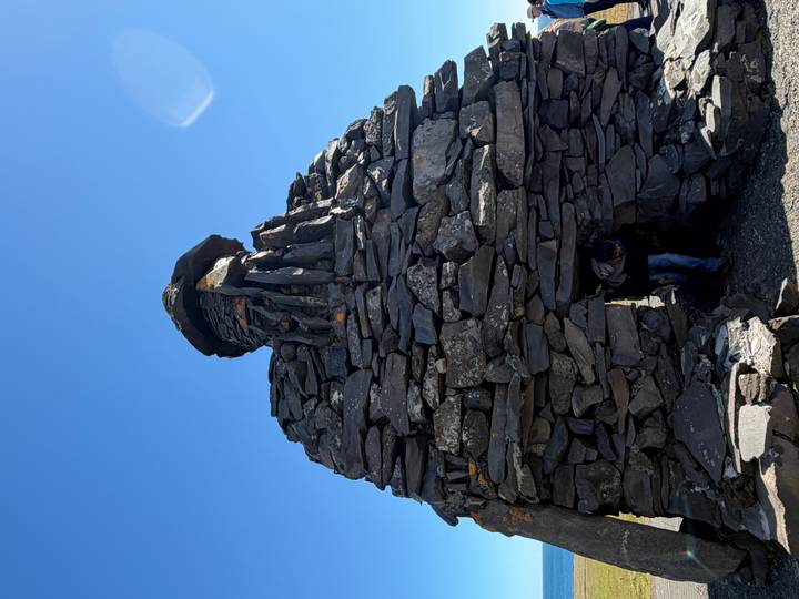 Large stone cairn monument with a traveller peeking from its small doorway under a clear sky