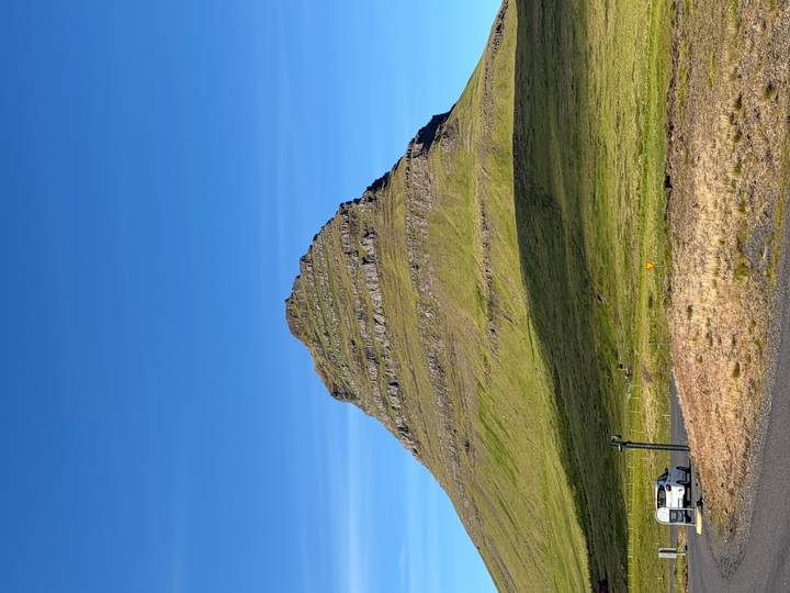 Iconic pyramid-shaped Kirkjufell mountain rising steeply above lush green fields under a clear blue sky