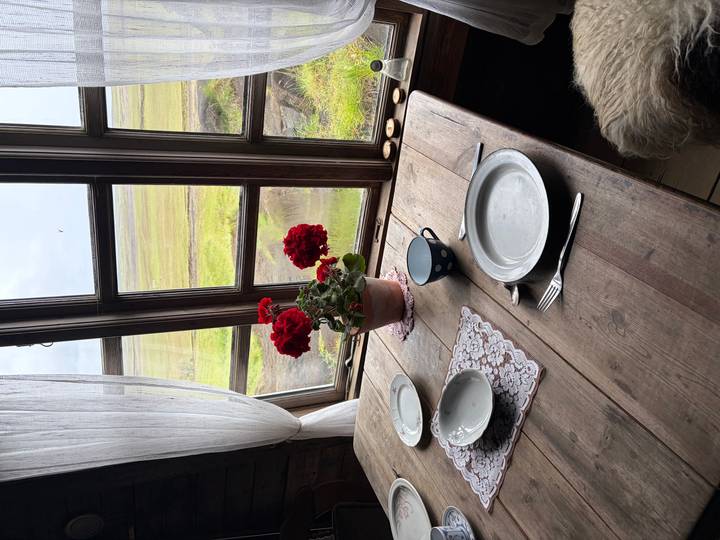 Rustic wooden table set for two beside a cottage window overlooking Icelandic marshland