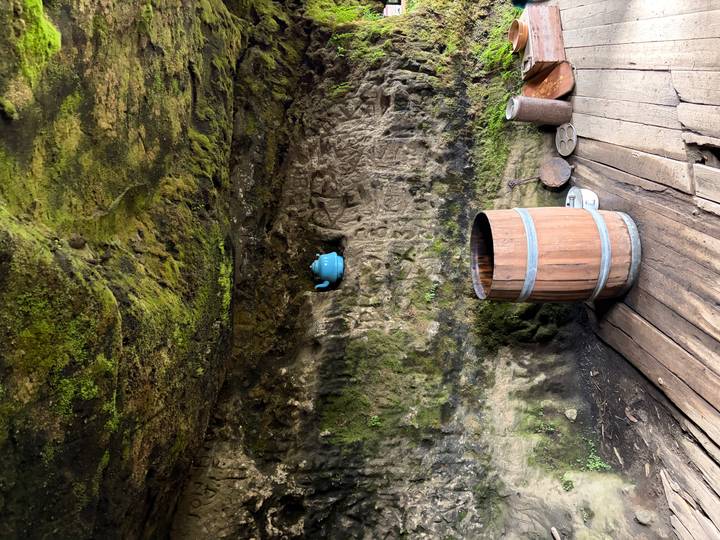 Mossy cave interior with an old wooden barrel and a blue teapot fixed to the rock wall