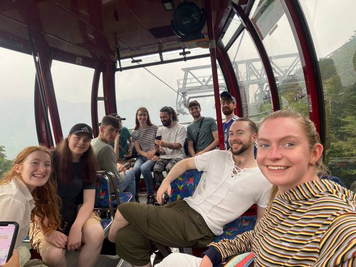 Large group smiling inside a red cable car ascending a misty mountain.