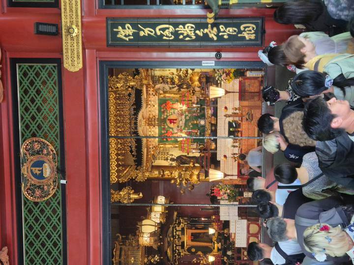 Crowds gather before an ornate golden altar inside a Japanese temple hall.