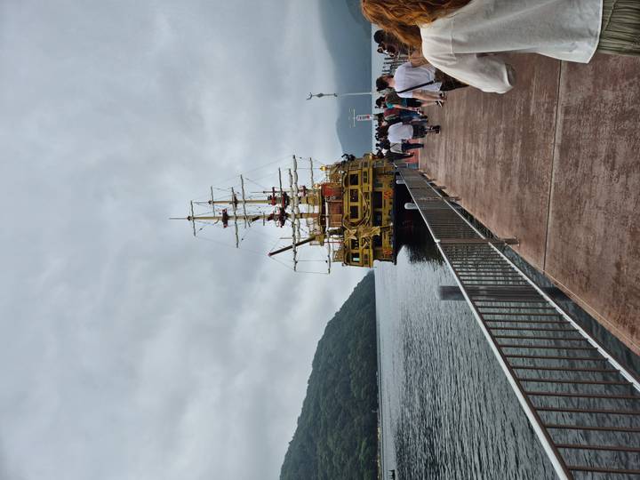 Yellow pirate-style sightseeing ship docked on a misty lake pier with passengers walking aboard.