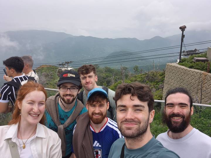Smiling friends at a foggy mountain lookout platform with cables overhead.