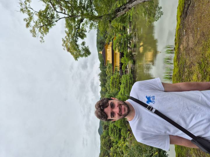 Visitor smiles beside the reflective pond of the Golden Pavilion temple in Kyoto.
