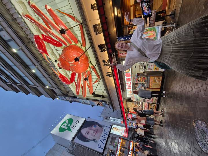 Traveller poses joyfully beneath the giant mechanical crab sign in lively Dotonbori street.