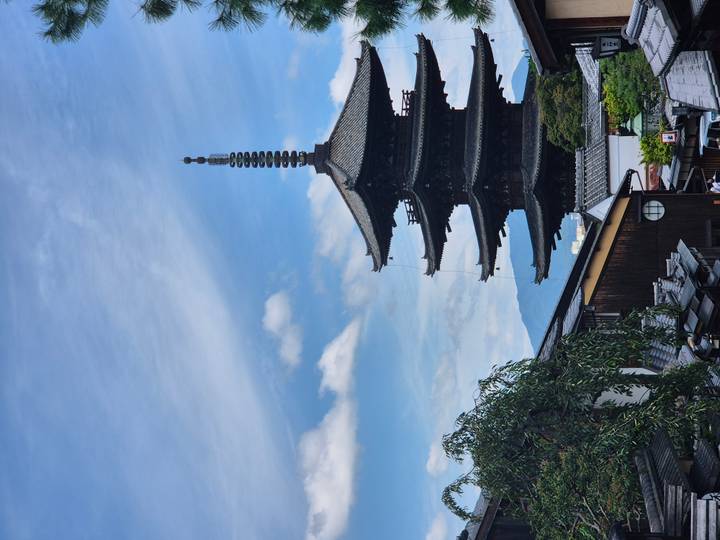 Five-story Yasaka pagoda rises above traditional wooden rooftops under a blue sky.