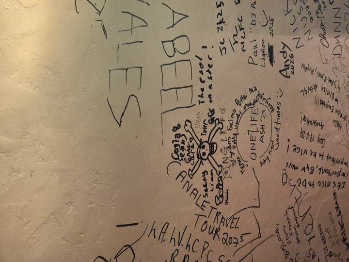 Interior wall covered with traveller graffiti and doodles under dim lighting.