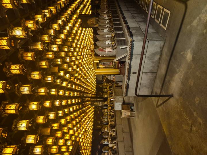 Hall filled with hundreds of glowing golden lanterns and stone statues in soft light.