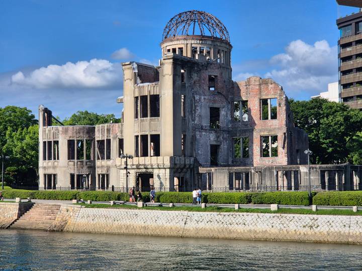 Historic A-Bomb Dome ruins stand beside a river under bright blue skies.