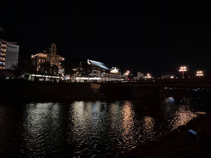 Bridge and riverside buildings softly lit and reflected on water in the dark night.