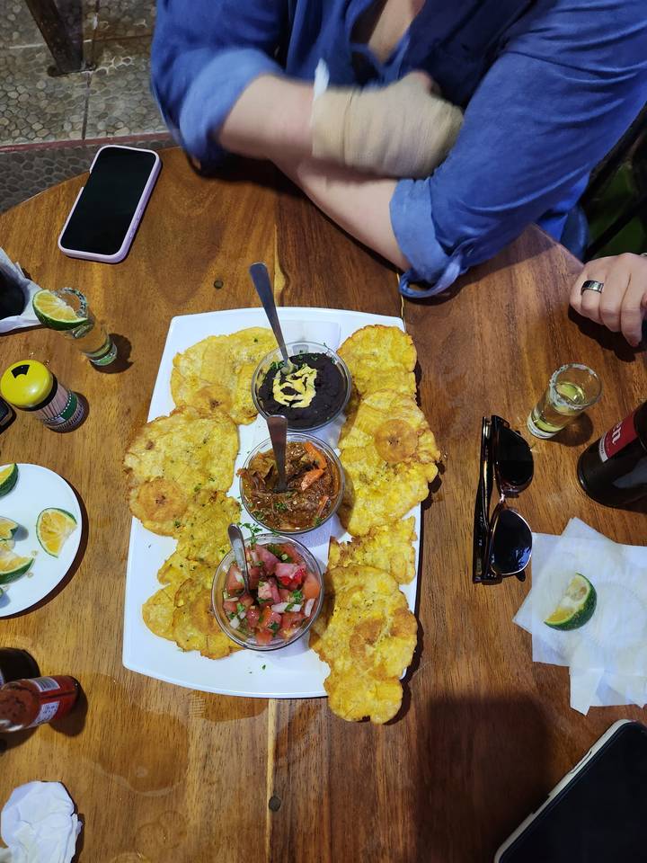 Costa Rican platter with plantain tostones, black beans, stew, and salsa shared around a wooden table.