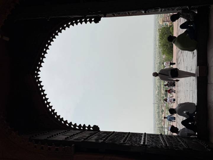 Silhouetted visitors framed by a massive arched gateway look out over Fatehpur Sikri plains.