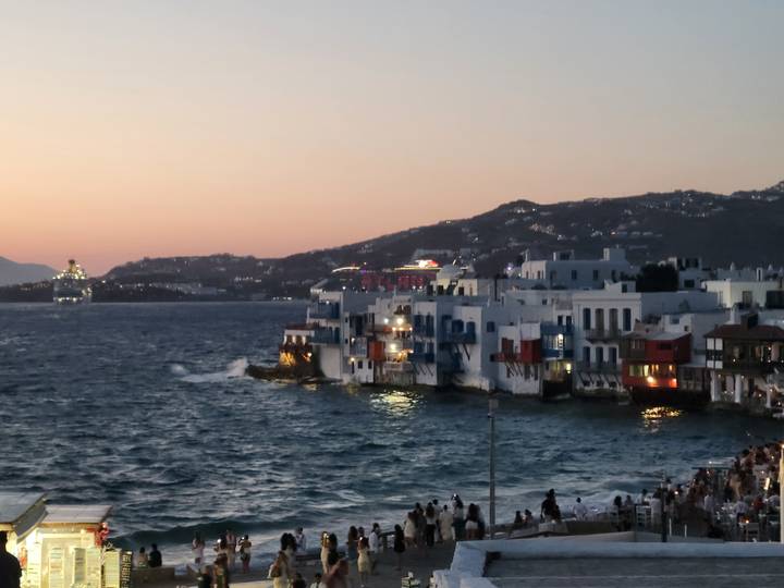 Whitewashed seafront houses with colorful balconies line the shore at dusk on a windy bay.