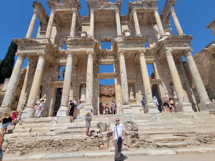 Visitors explore the grand marble façade and columns of the Library of Celsus on a sunny day.