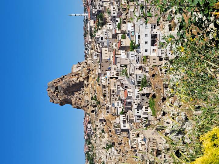 Rock citadel towers above a sprawling Cappadocia village on a bright summer day.
