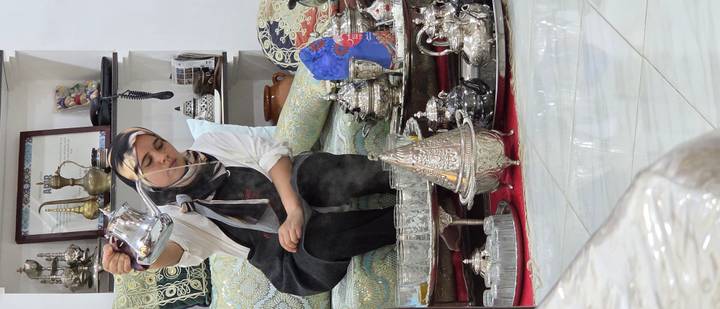 Woman expertly pouring steaming mint tea in a silver service shop filled with ornate teapots.