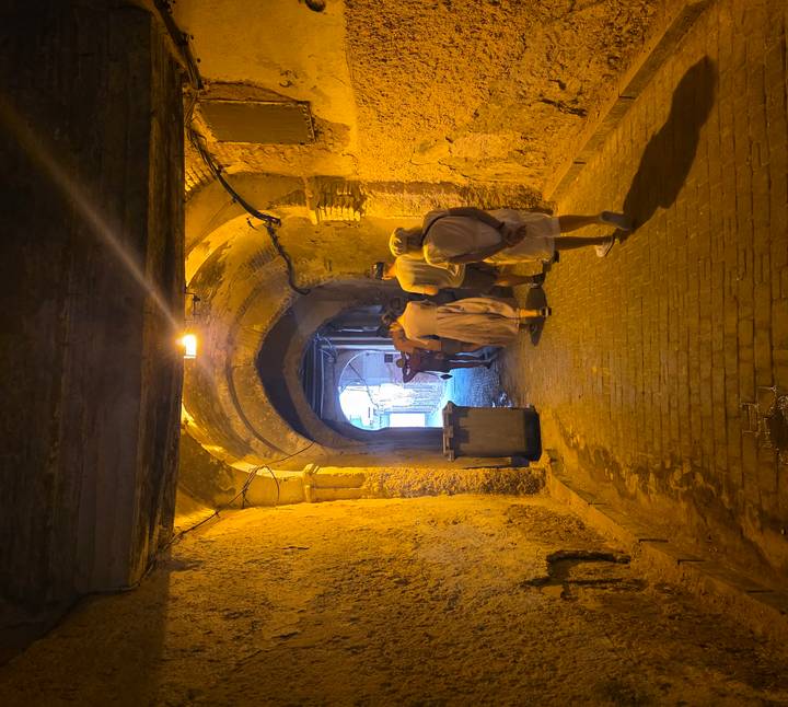 Dimly lit arched tunnel in an old medina with tourists walking toward the exit.