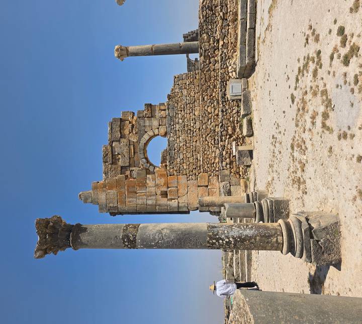 Ancient Roman stone arch and weathered columns standing amid archaeological ruins under a clear sky.