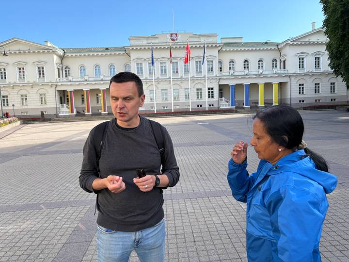 Local guide explains history to a visitor outside a neoclassical government building in Vilnius.