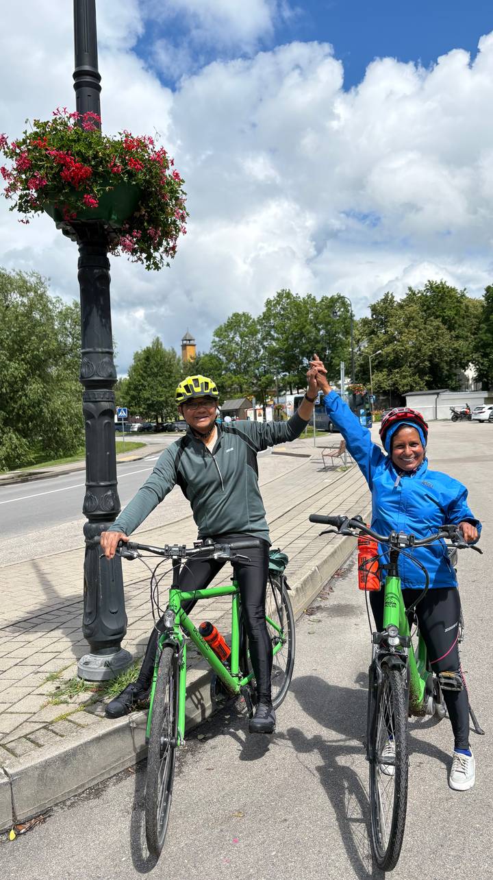Two cyclists celebrate holding hands beside their bikes on a small town street.