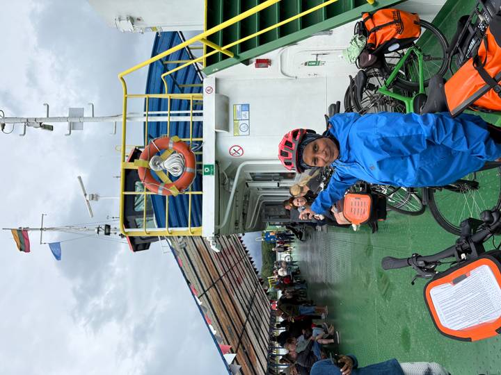 Traveller in blue rain jacket points while standing aboard a bicycle ferry deck.