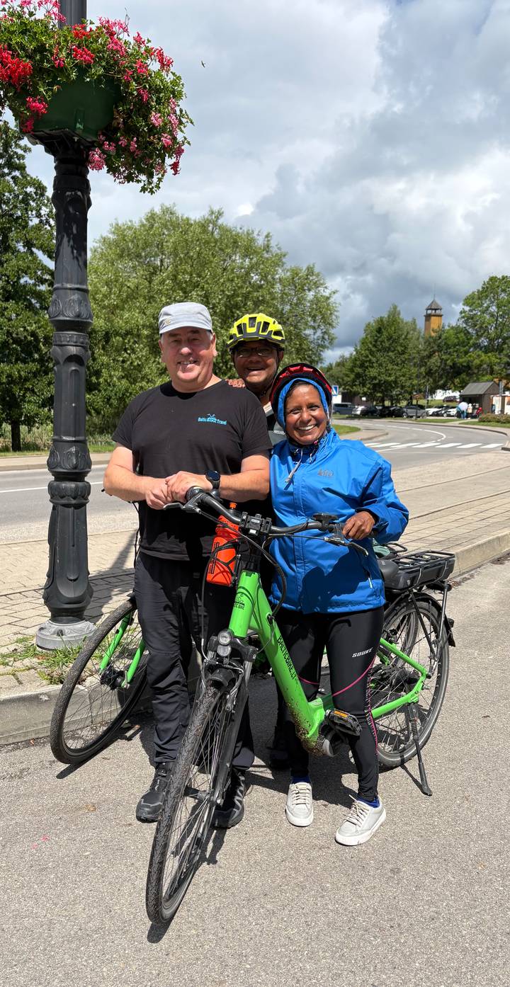 Cyclists pose with green e-bikes on a roadside under sunny skies.