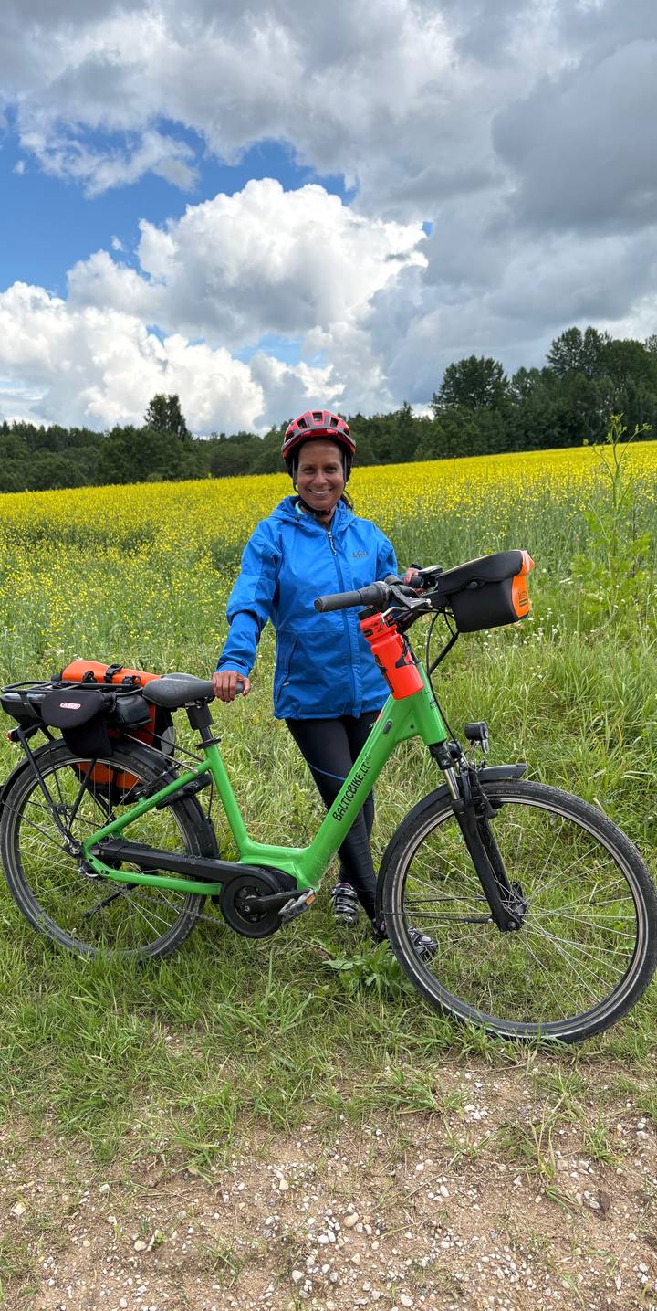 Cyclist pauses with a green bike beside a vibrant yellow rapeseed field and tall grass in the countryside.