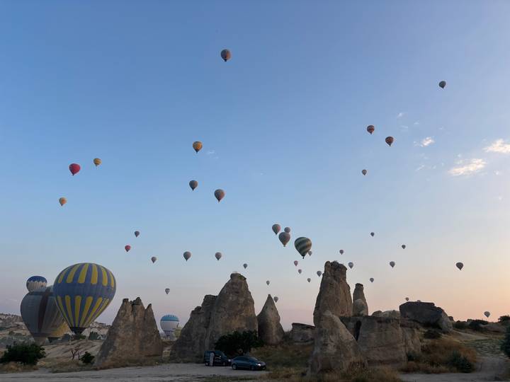Dozens of colorful hot-air balloons rise over Cappadocia’s rock spires at dawn beneath a pastel sky.